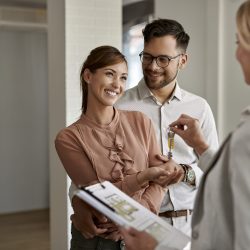 Happy couple buying new home and receiving house keys form real estate agent.